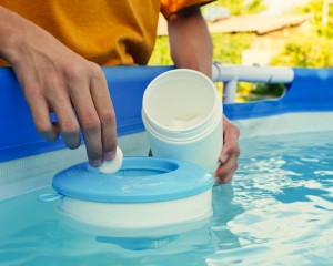 Person adding pool chemicals into their pool water.